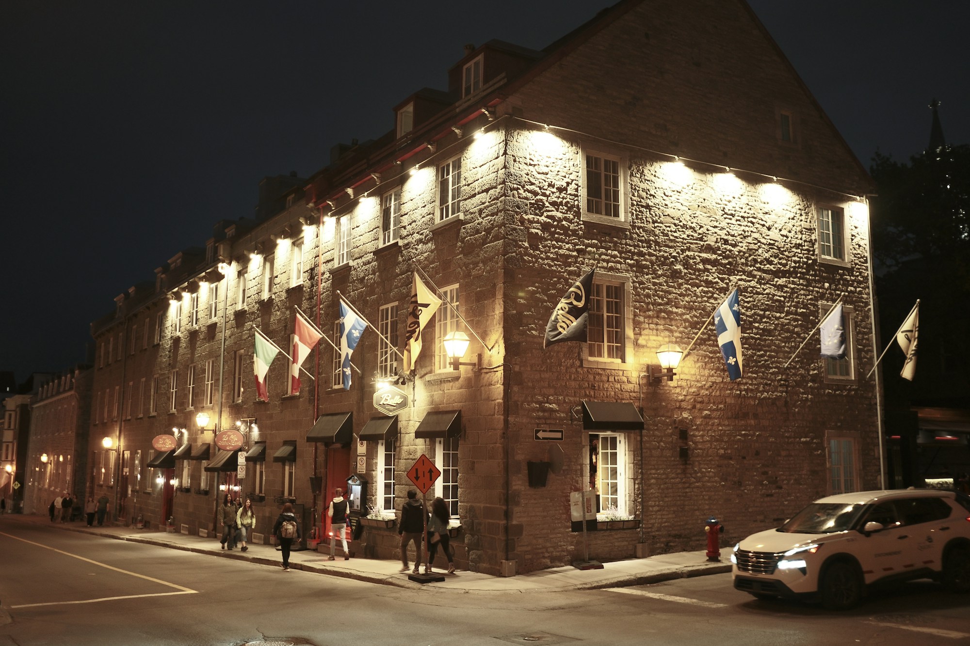 Ein beleuchtetes Steingebäude bei Nacht im Vieux-Québec, Fahnen an den Fenstern