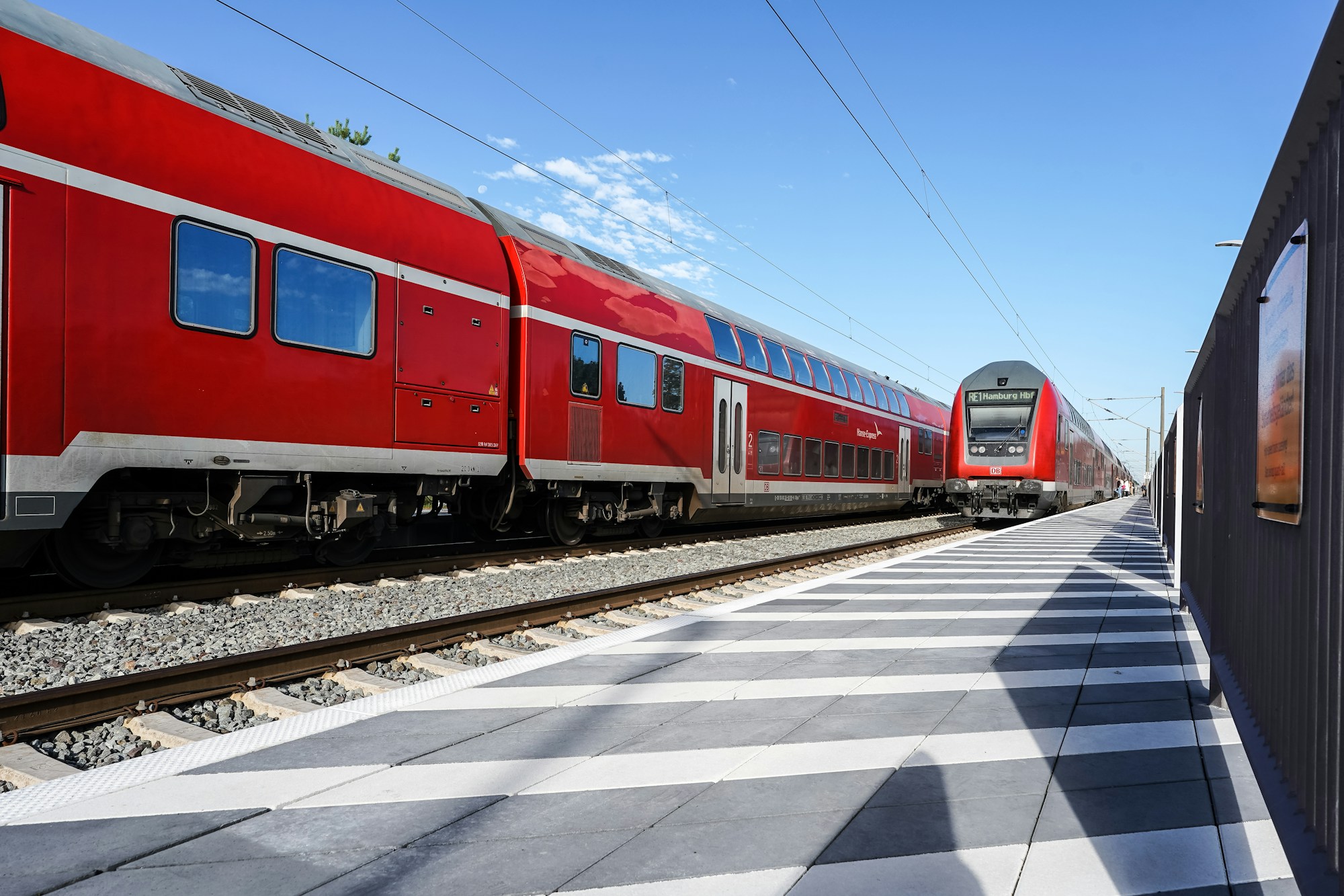 Zwei rote Doppelstock-Regionalzüge am Bahnsteig unter blauem Himmel