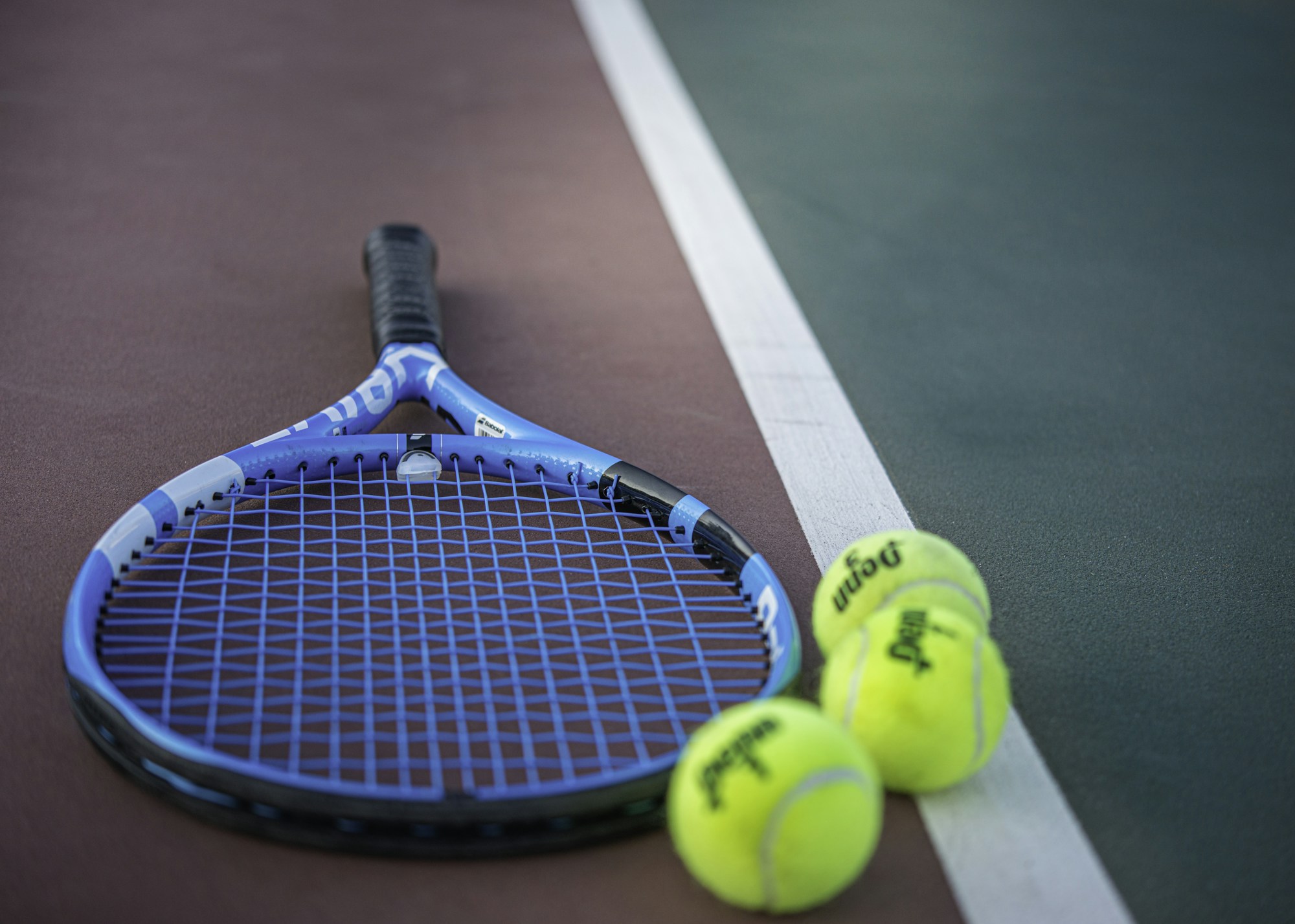 Raquette de tennis jaune et bleue et balles posées sur un court, prêtes pour un tournoi en salle