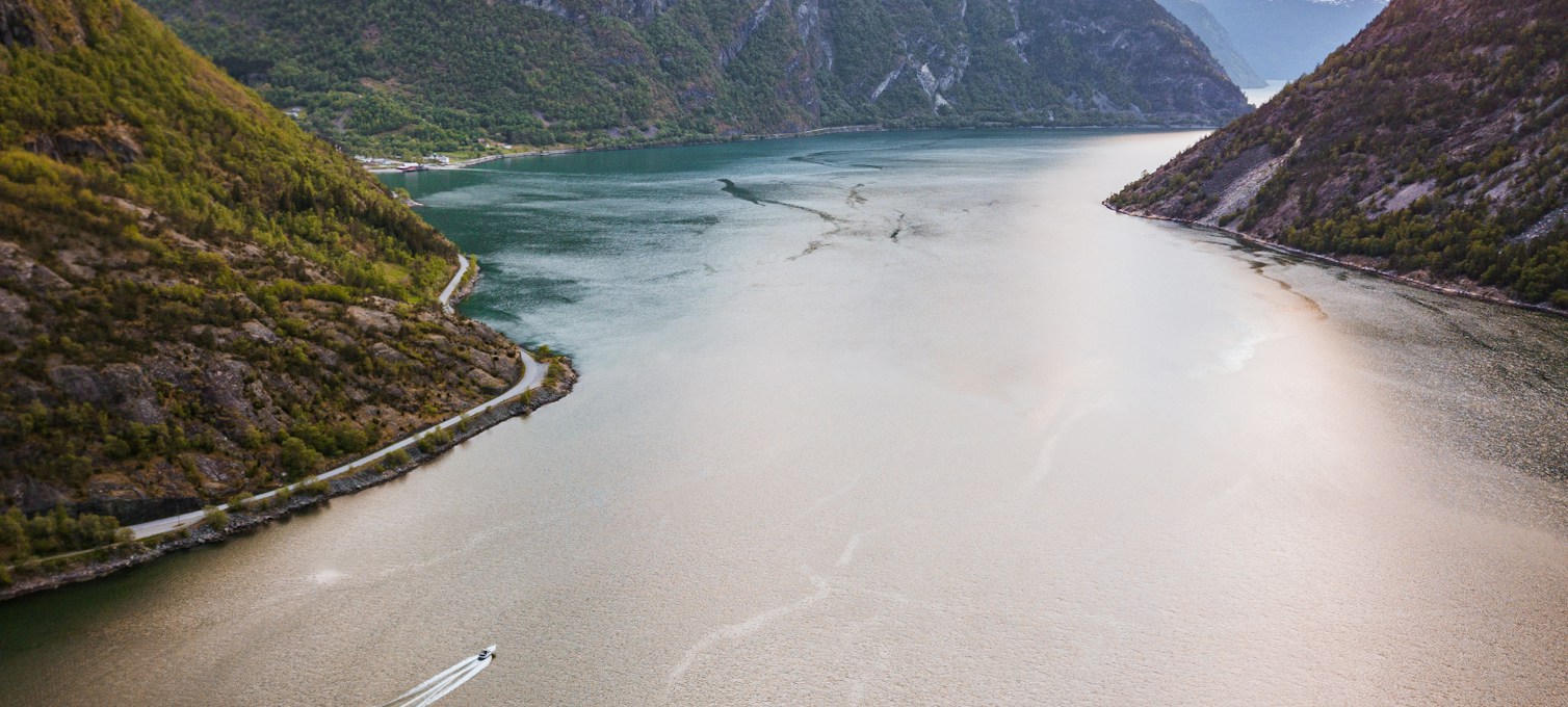 Norwegian fjord between mountain walls, coastal road and boat on the water