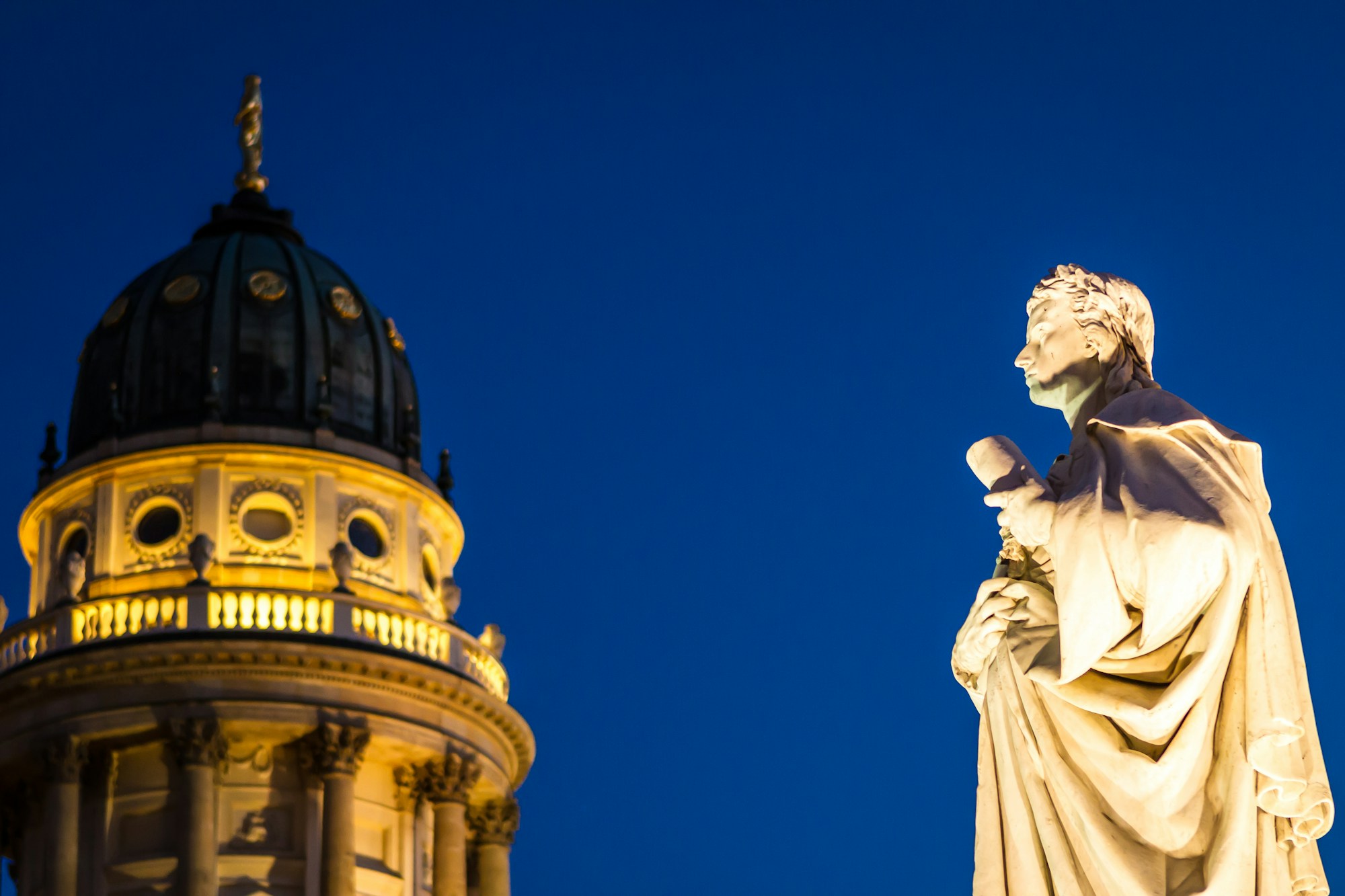 Illuminated dome of the Französischer Dom and statue of Schiller on the Gendarmenmarkt square in Berlin, at night