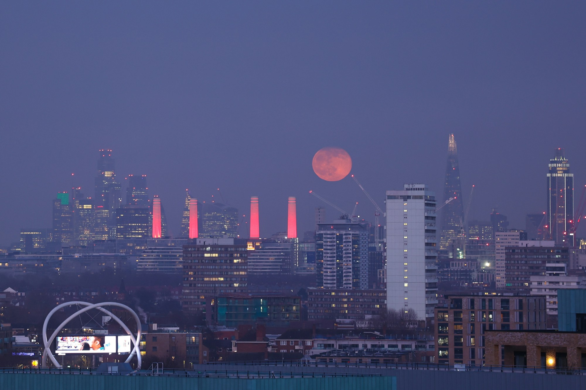 Lune pleine orangée qui se lève au-dessus de la skyline de Londres au crépuscule