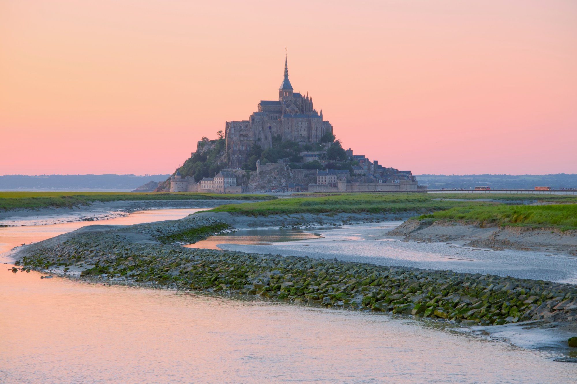 Mont-Saint-Michel dans la baie au crépuscule, ciel rose et chenaux de marée