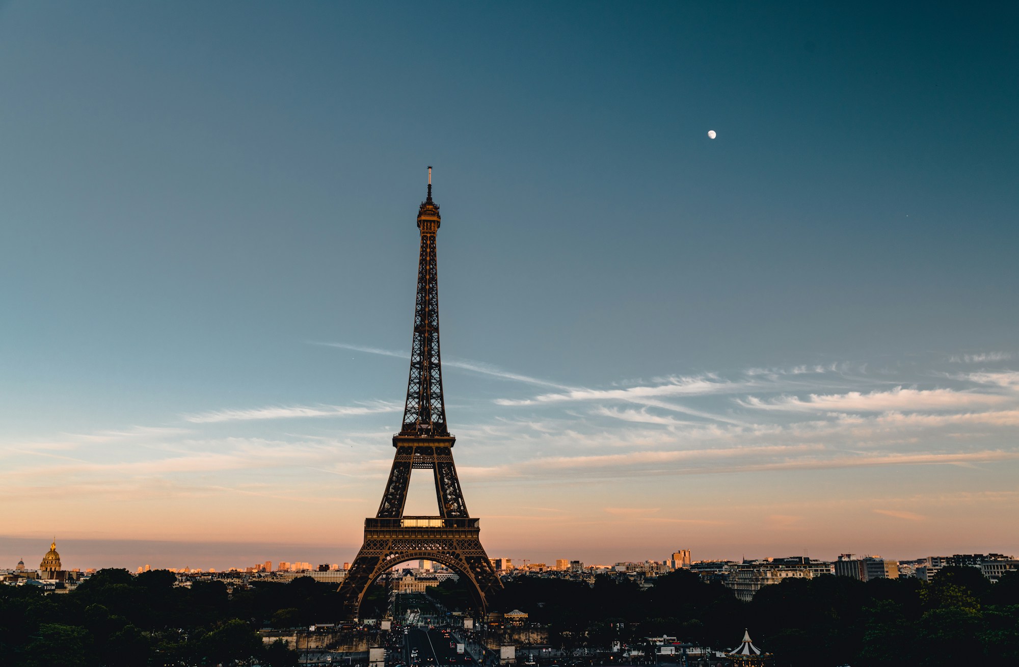 Tour Eiffel au crépuscule avec la Lune haute dans un ciel dégradé orange et bleu