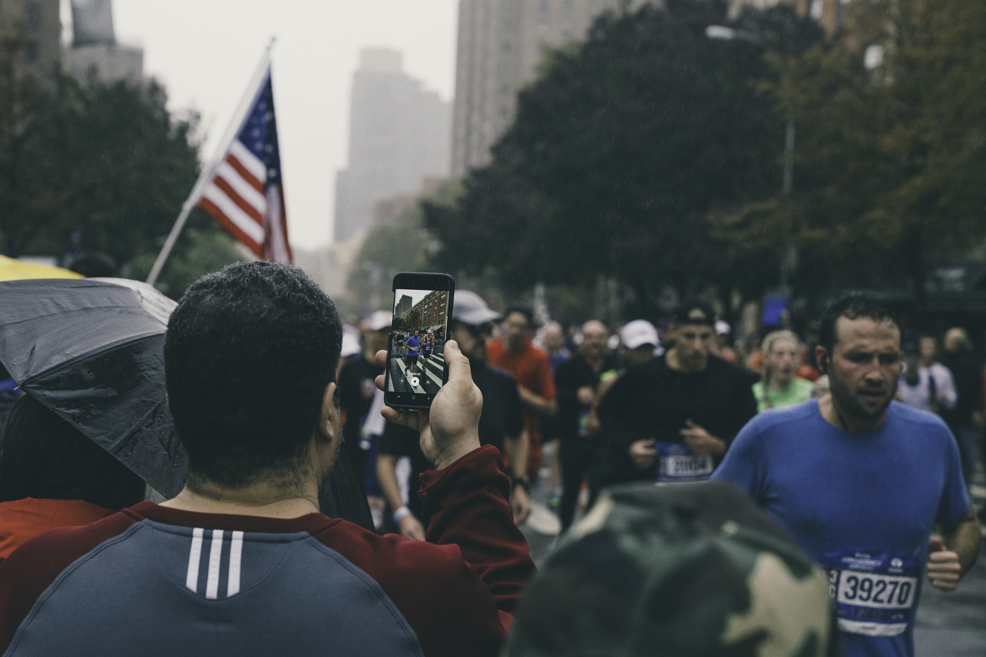 Spectator filming marathon runners near the north-east corner of Central Park in New York