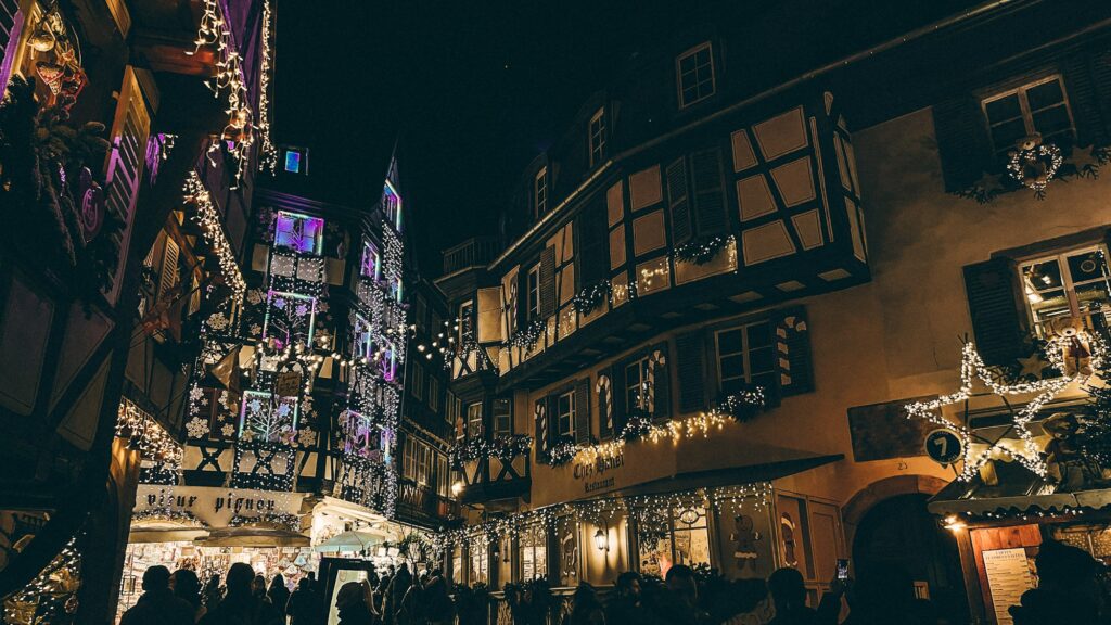 Rue de Colmar décorée de guirlandes de Noël la nuit, devant des maisons à colombages