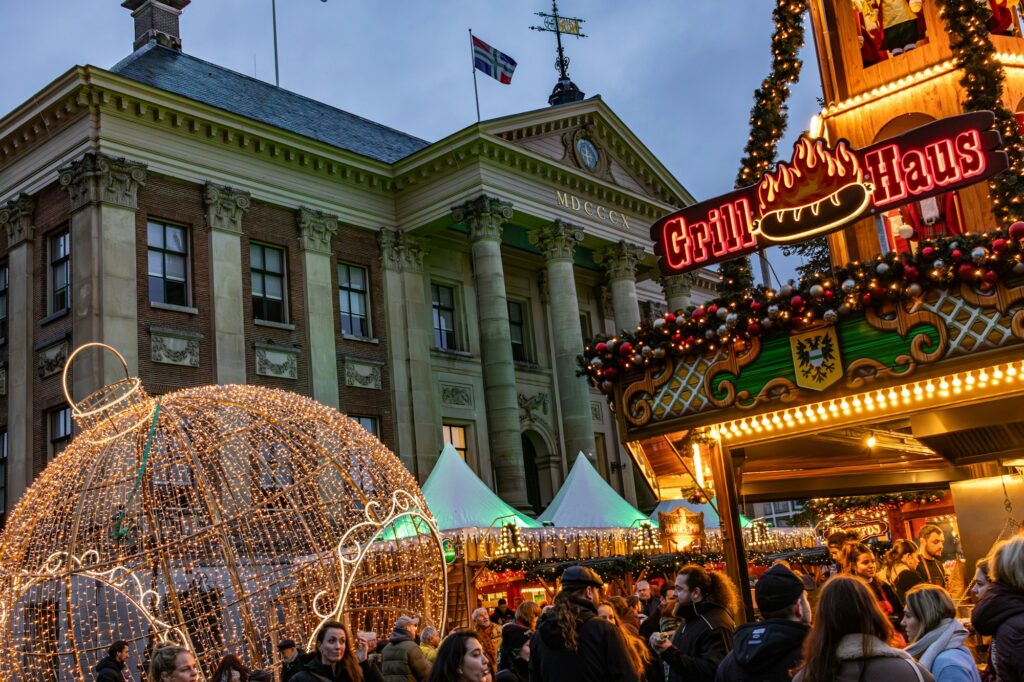 Marché de Noël néerlandais illuminé à Groningen, avec étals éclairés et grande sphère lumineuse devant une façade historique