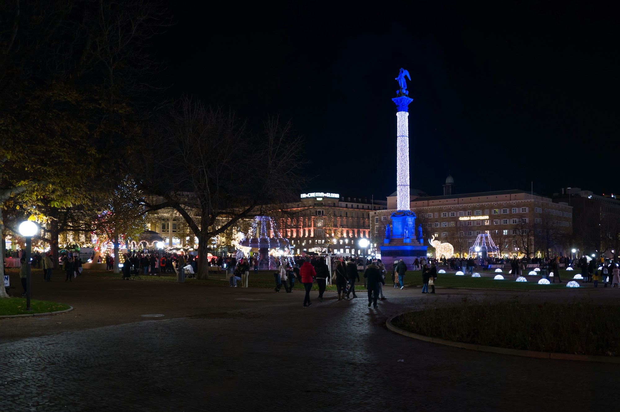 Vista nocturna de la plaza Schlossplatz de Stuttgart durante el mercado de Navidad, con una columna iluminada