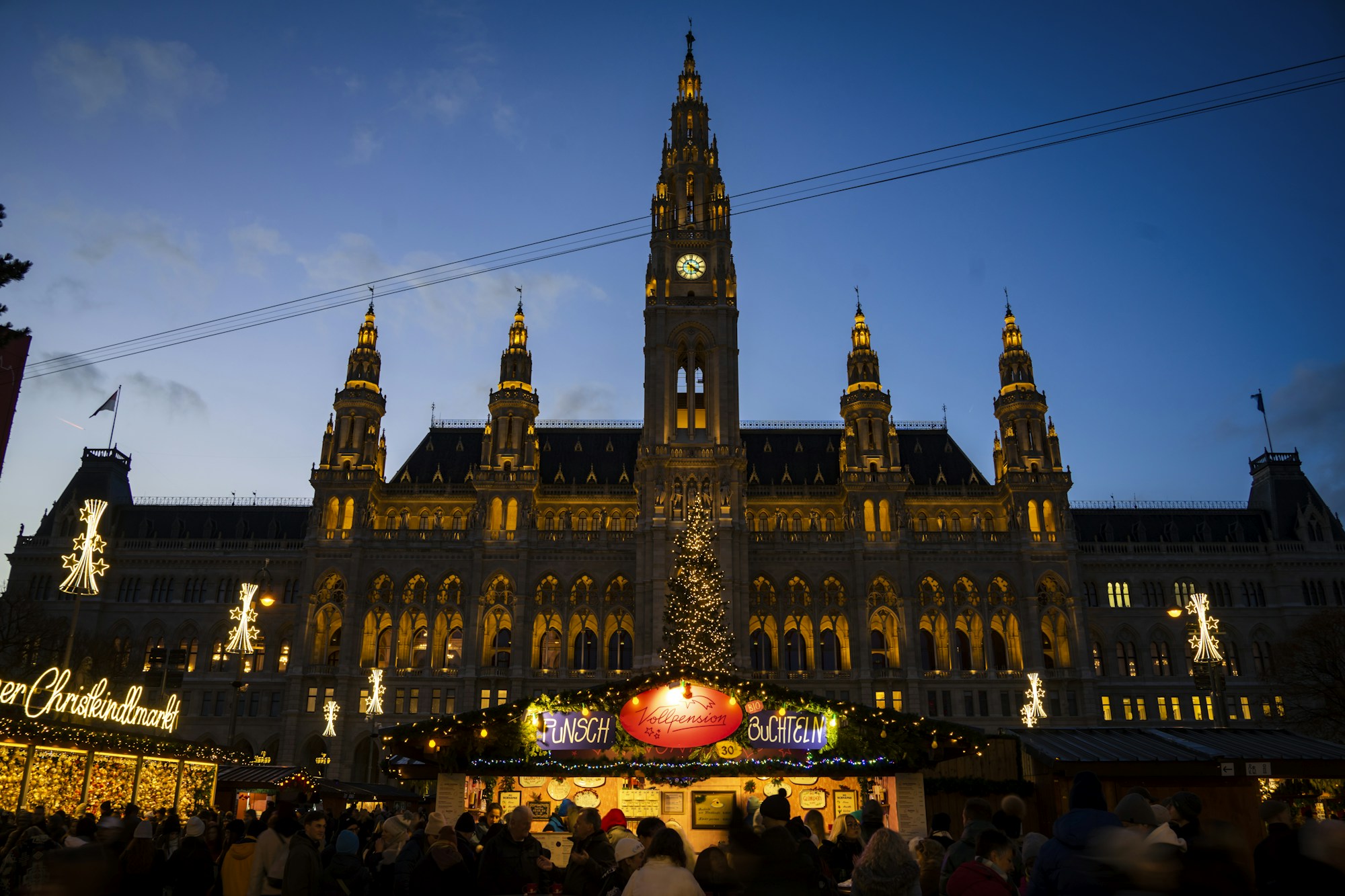 Lit-up stalls of the Rathausplatz Christmas market in front of Vienna's City Hall at dusk
