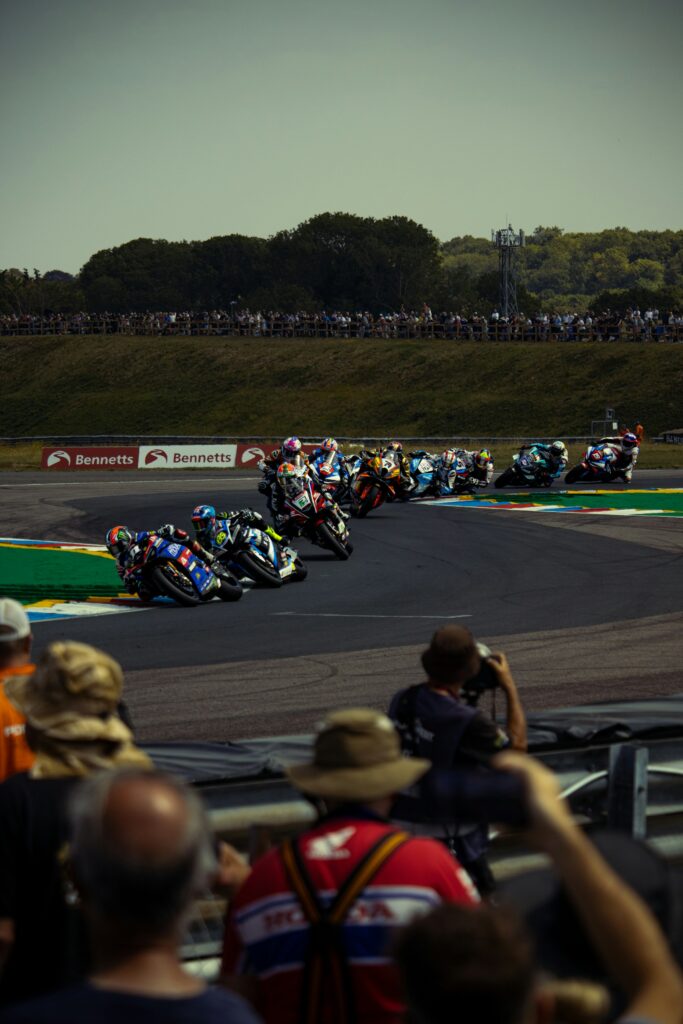 Motos de course qui prennent un virage sur un circuit, avec des spectateurs dans les tribunes
