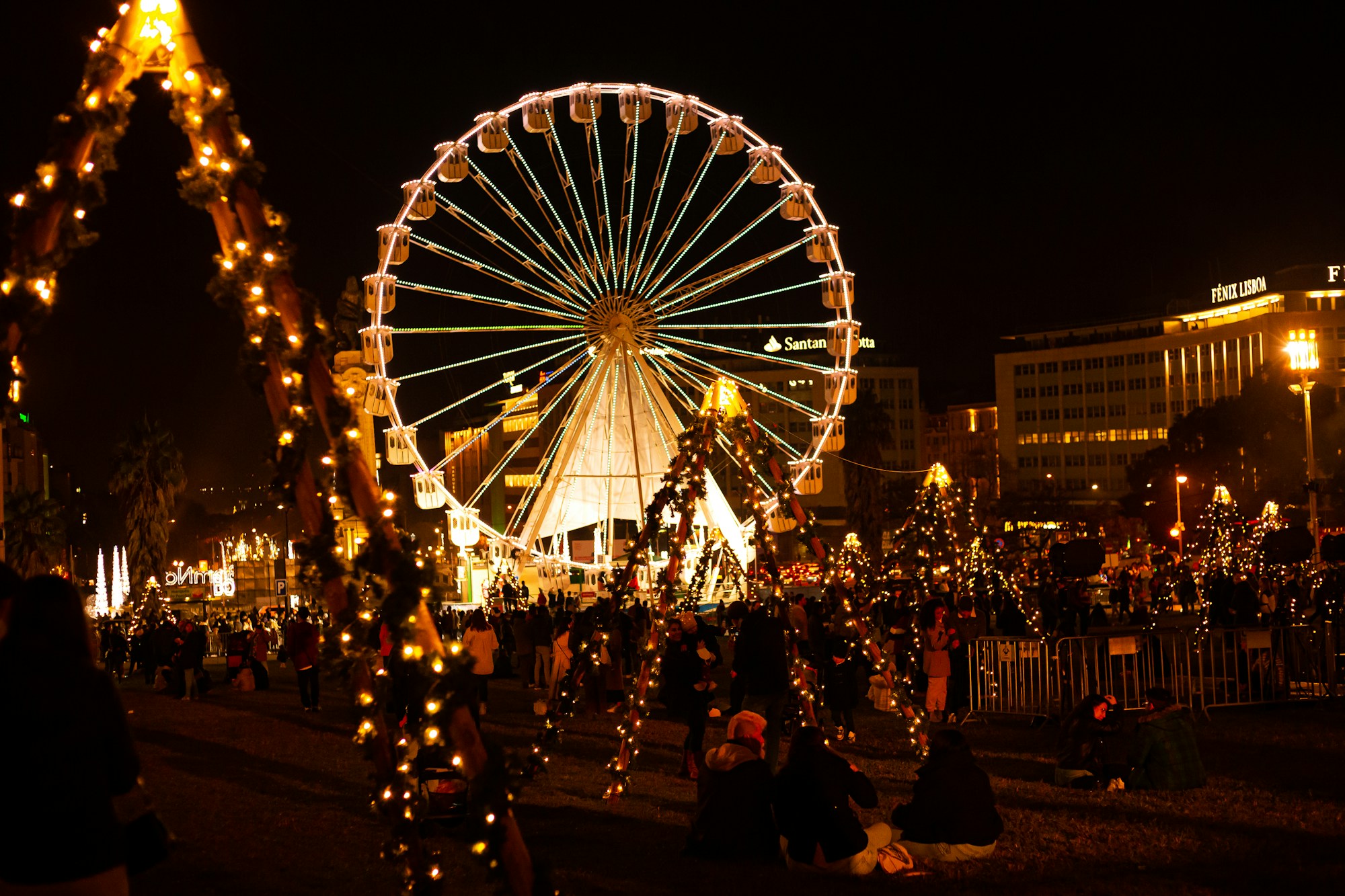 Grande roue illuminée de guirlandes de Noël à Lisbonne, la nuit, avec la foule au pied de la roue