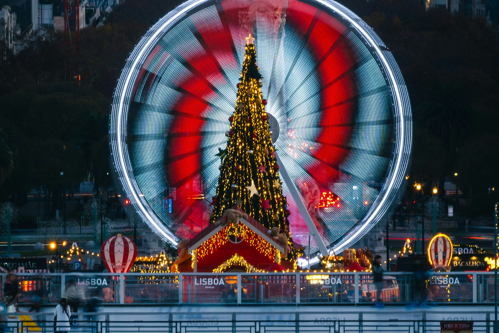 Sapin de Noël illuminé devant la grande roue sur une place de Lisbonne, au crépuscule
