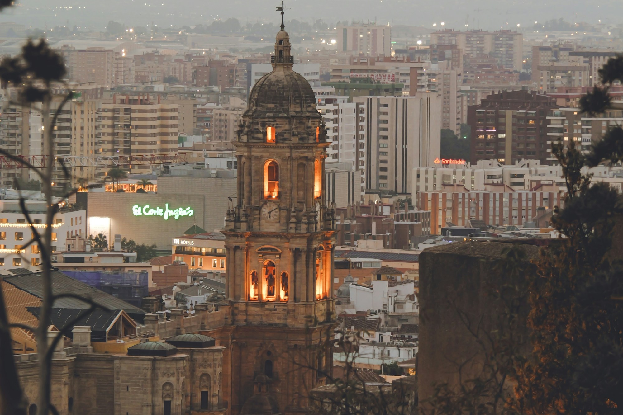 Cathedral tower in Málaga lit at dusk, seen from the high ground of the city