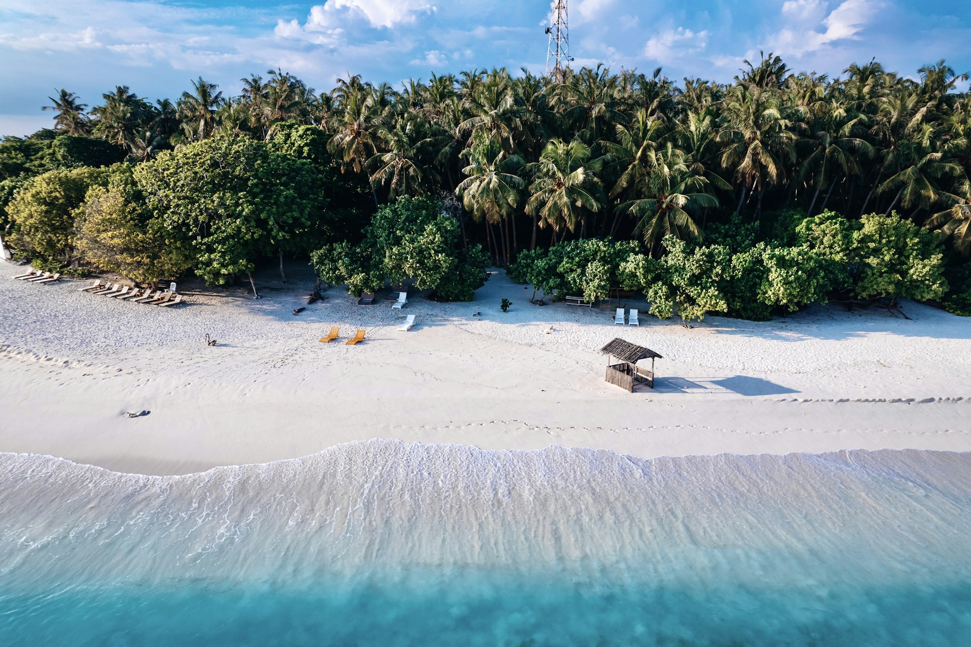 Aerial view of a white sand beach lined with palm trees and turquoise water on Kamadhoo, Maldives