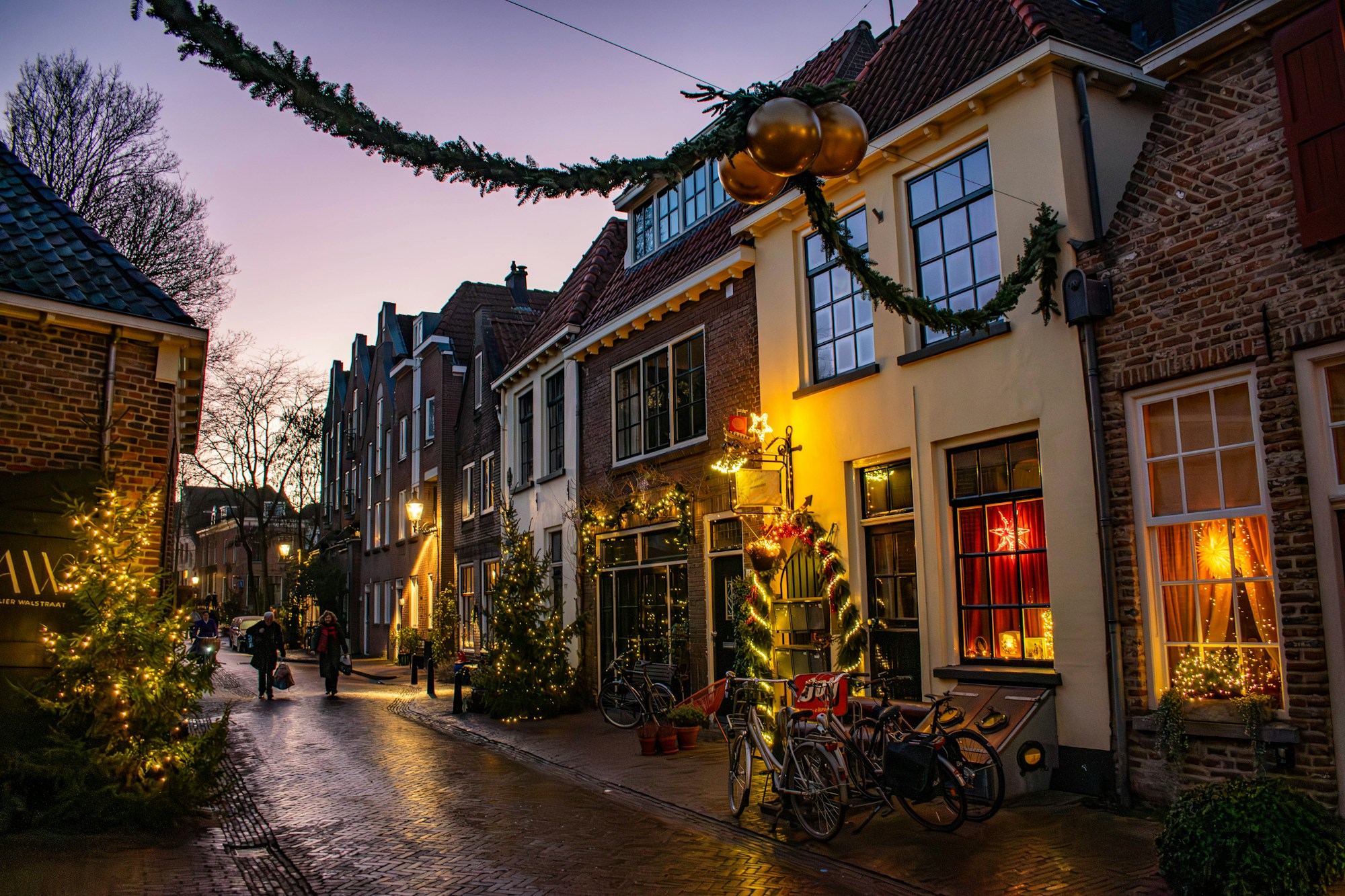 Festlich geschmückte niederländische Straße in der Dämmerung, mit Girlanden, goldenen Kugeln und beleuchteten Schaufenstern in Deventer