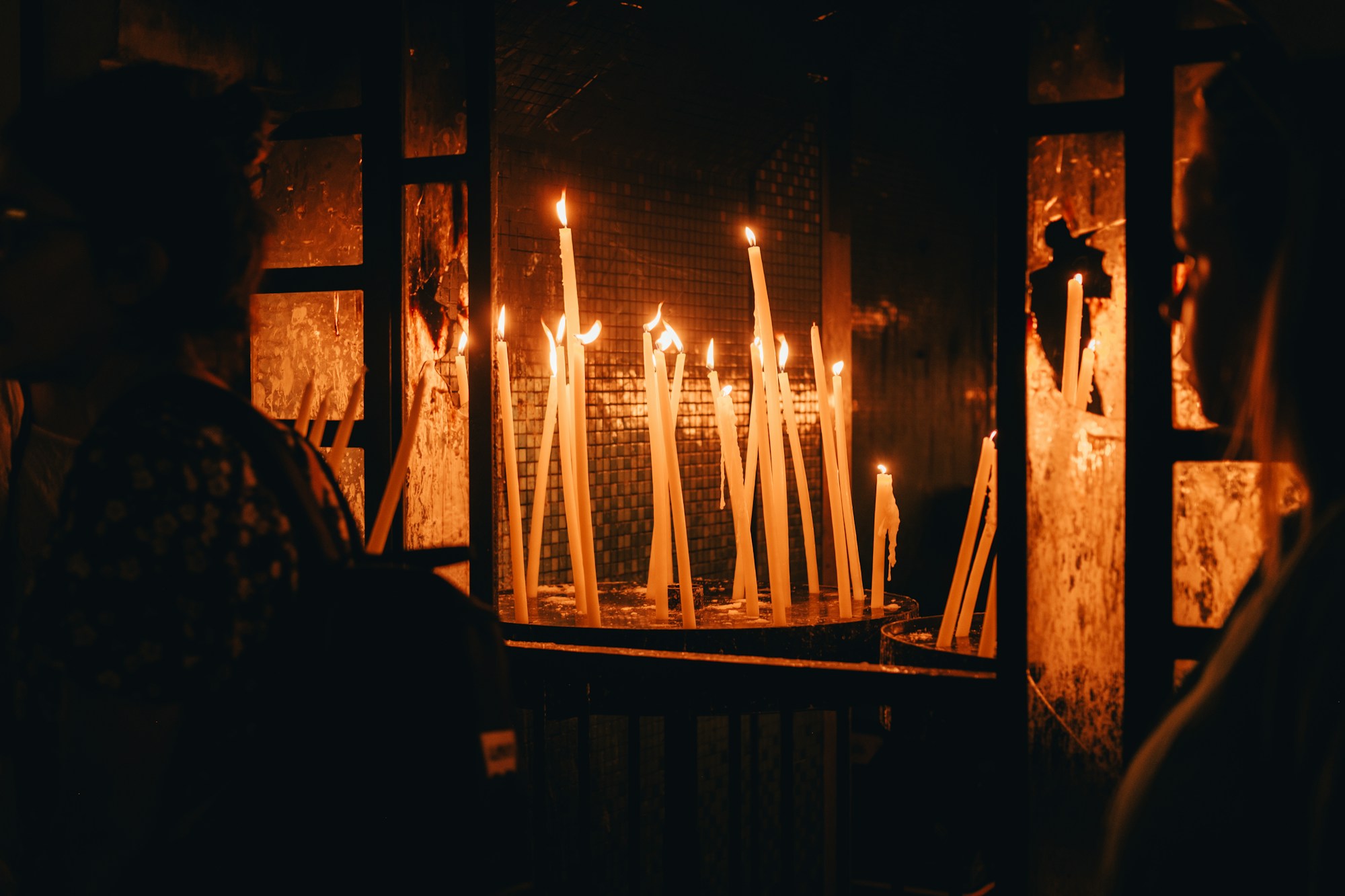 Velas encendidas delante de fieles, en la penumbra de un santuario