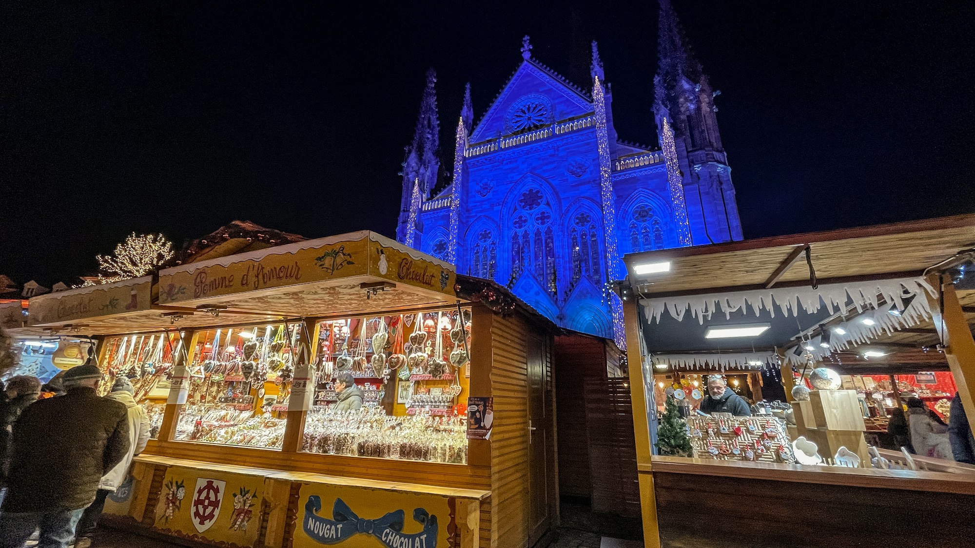 Casetas de madera de un mercado de Navidad iluminadas por la noche, delante de una iglesia gótica iluminada