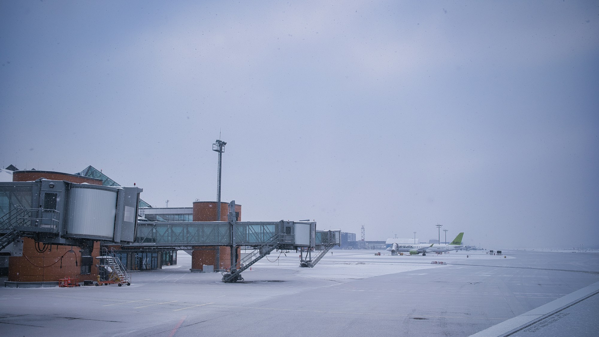 Fluggastbrücken und ein Flugzeug in der Ferne auf einem verschneiten Vorfeld im Winter