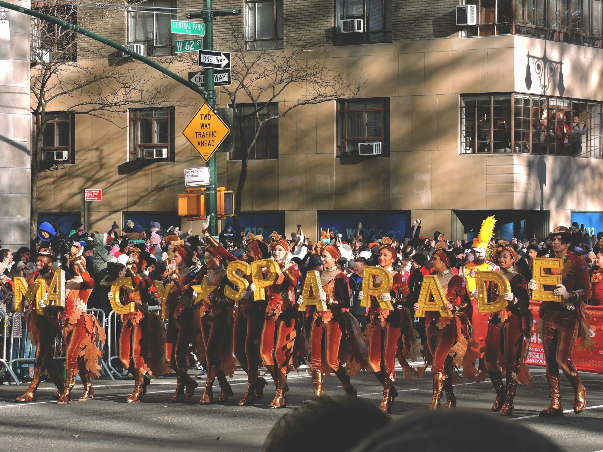 Kostümierte Teilnehmer marschieren vor den goldenen Lettern MACY'S THANKSGIVING DAY PARADE an der Central Park West