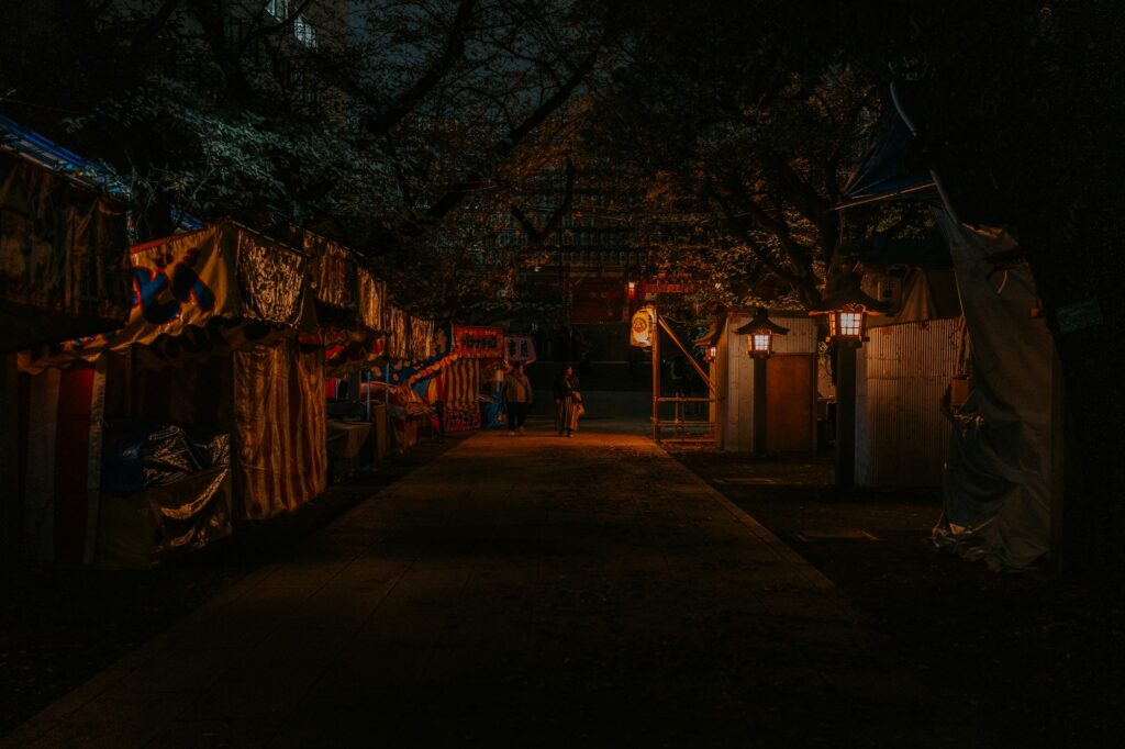 Allée nocturne bordée d'étals couverts de bâches et de lanternes, lors d'une fête de sanctuaire à Tokyo