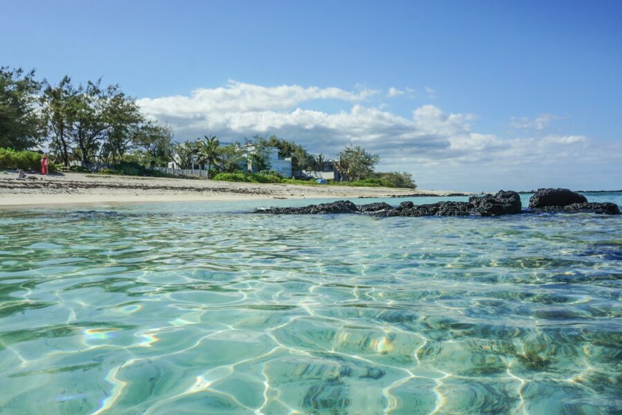 Plage de sable aux eaux turquoise transparentes sur l'île Maurice, avec une maison blanche au loin