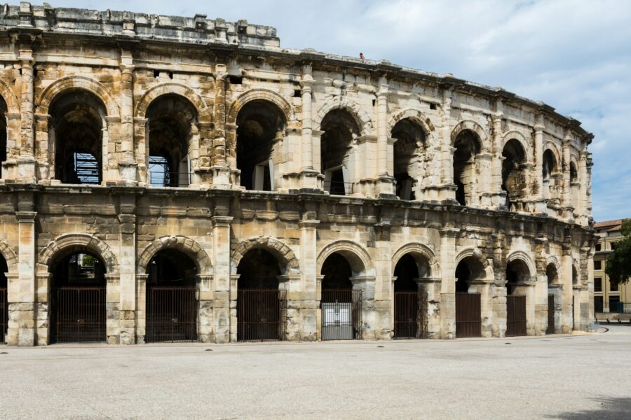 Façade en pierre de l'amphithéâtre romain de Nîmes sous un ciel clair, avec ses deux étages d'arcades