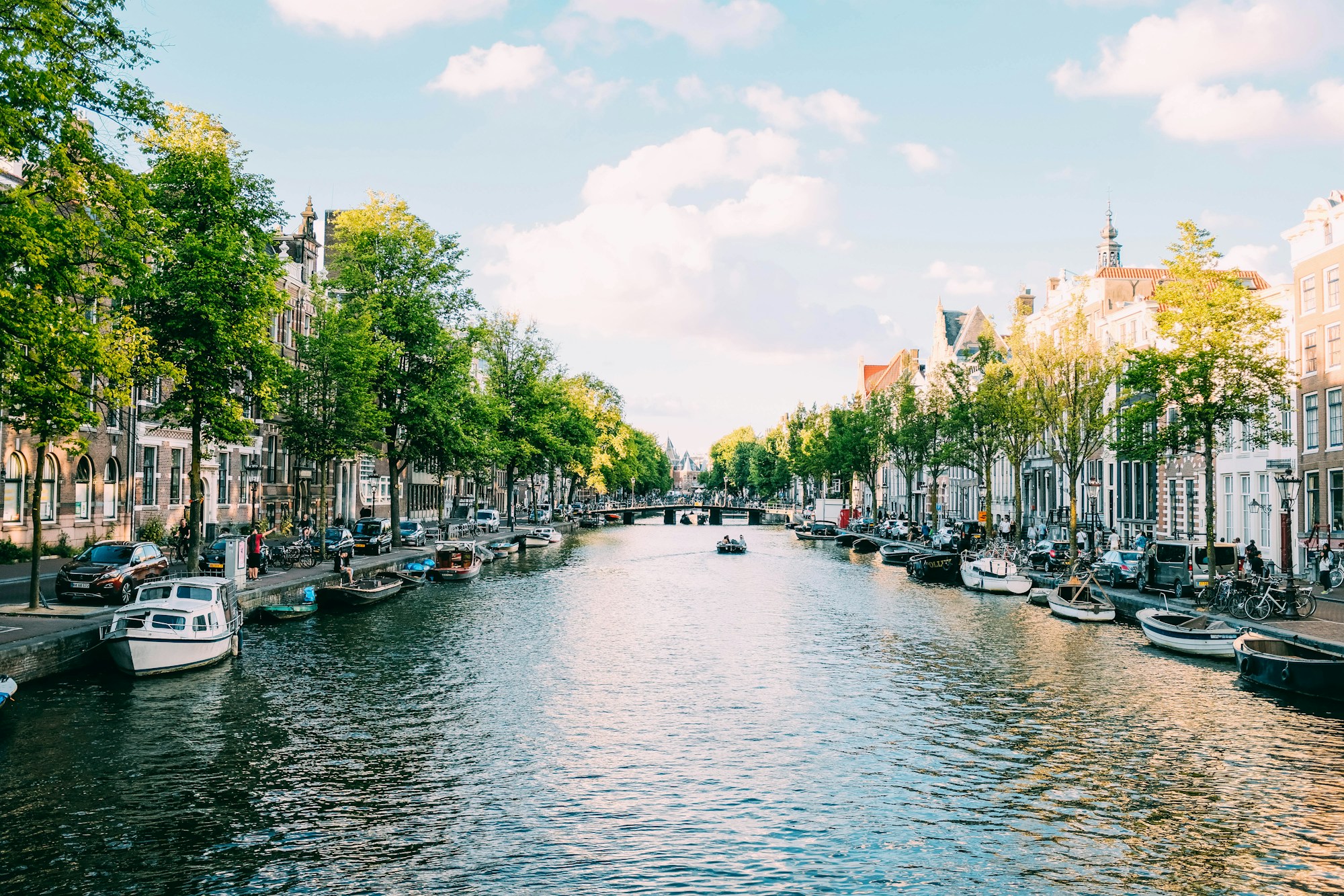 Boote, die an einem von Bäumen und alten Häusern gesäumten Kanal in Amsterdam festgemacht sind