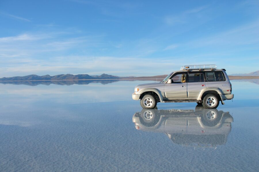 Un 4x4 se reflète dans la fine couche d'eau du Salar d'Uyuni sous un ciel bleu, Bolivie