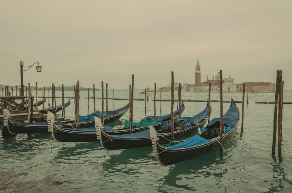 Gondolas lined up at the docks in Venice with calm water and the city behind