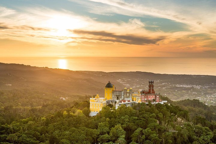 Pena Palace in Sintra at sunset, seen from above the forest with the sea on the horizon