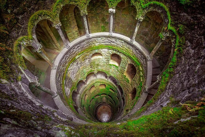 The spiral Initiation Well at Quinta da Regaleira in Sintra, its stone steps covered in moss