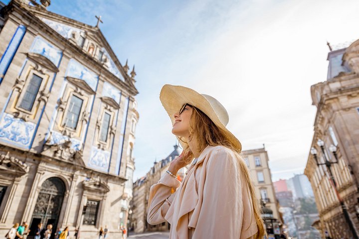 A woman in a sun hat in front of a blue-tiled church in the old town of Porto