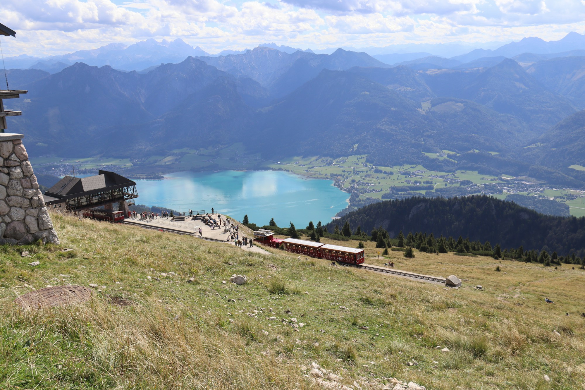 Un train rouge sur les pentes herbeuses du Schafberg, au-dessus d'un lac turquoise