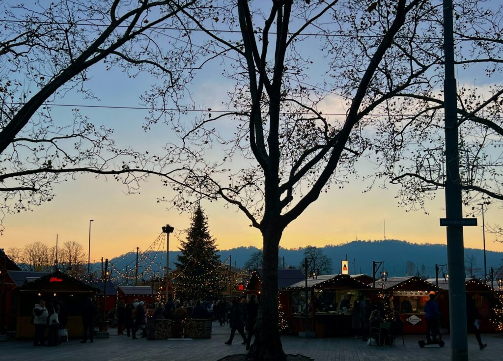 Chalets en bois éclairés d'un marché de Noël au crépuscule, avec sapin et caténaire de tram