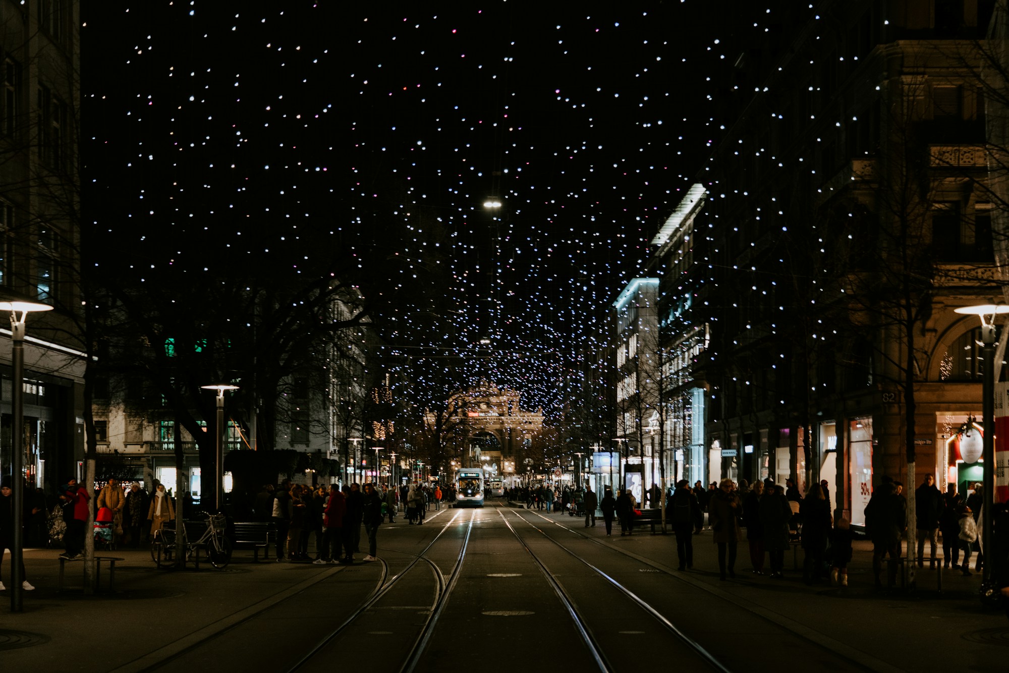 Rue illuminée de guirlandes lumineuses le soir, avec passants