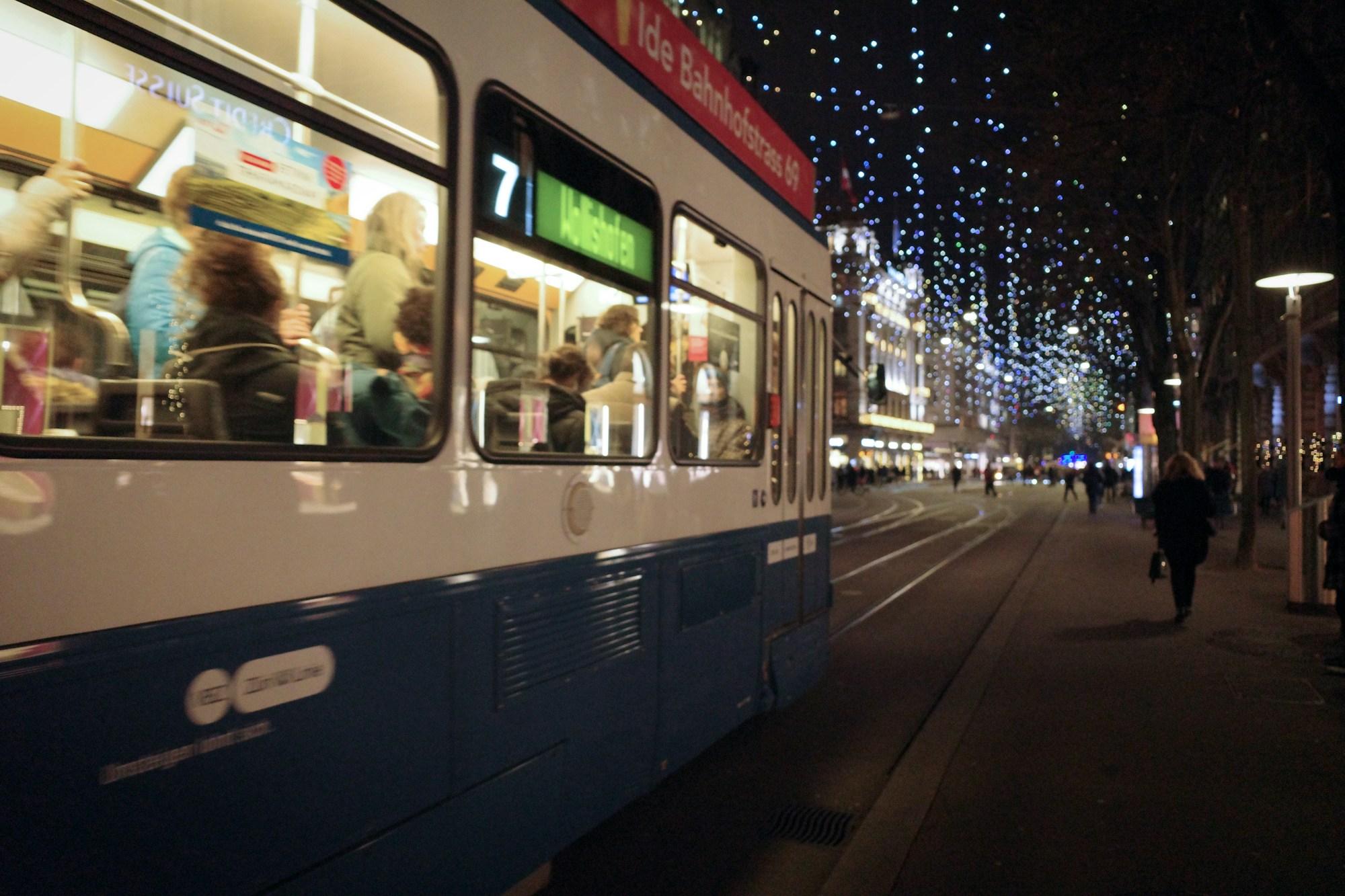 Tram bleu et blanc dans une rue illuminée pour Noël le soir
