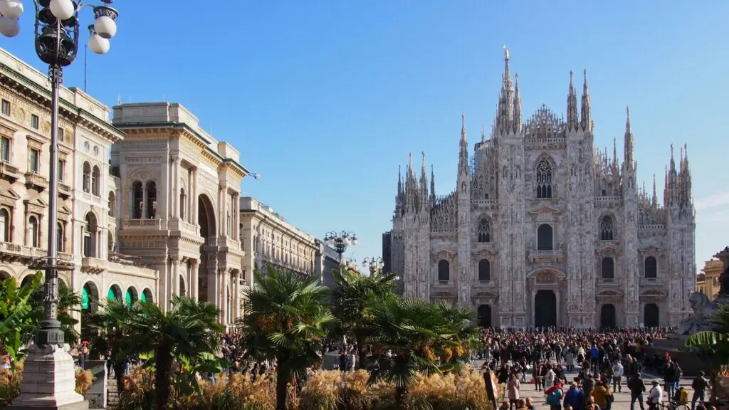 Foule de visiteurs devant le Duomo de Milan un jour d'été, sous un ciel bleu et des palmiers
