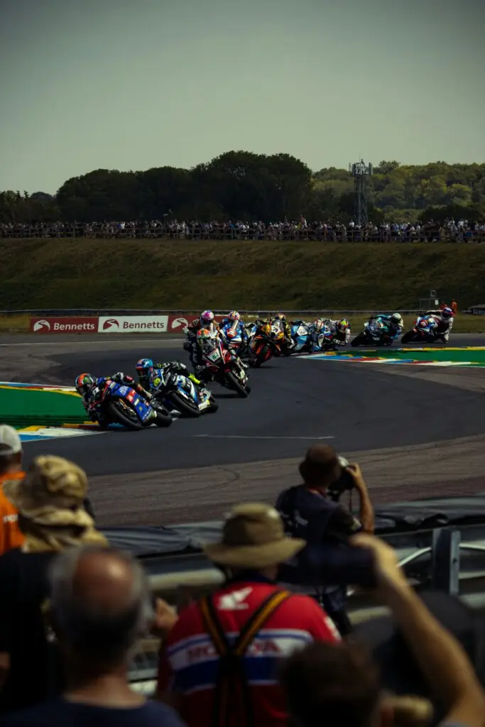 Motos de course qui prennent un virage sur un circuit, avec des spectateurs dans les tribunes