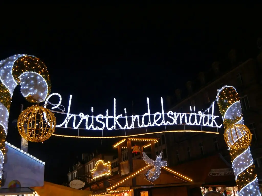 Un grand sapin illuminé en or et blanc au marché de Noël de Strasbourg, entouré de chalets