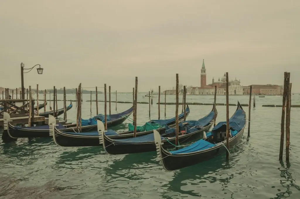 Gondolas lined up at the docks in Venice with calm water and the city behind